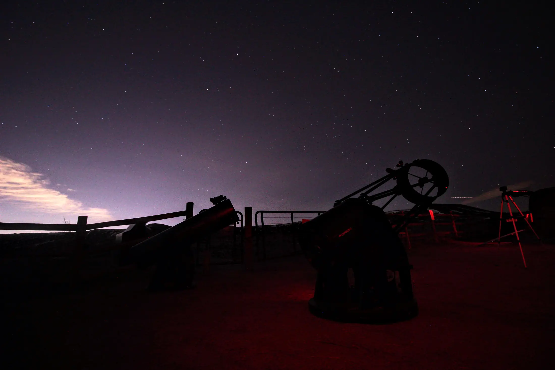 Telescopes silhouetted beside a fence under the night sky