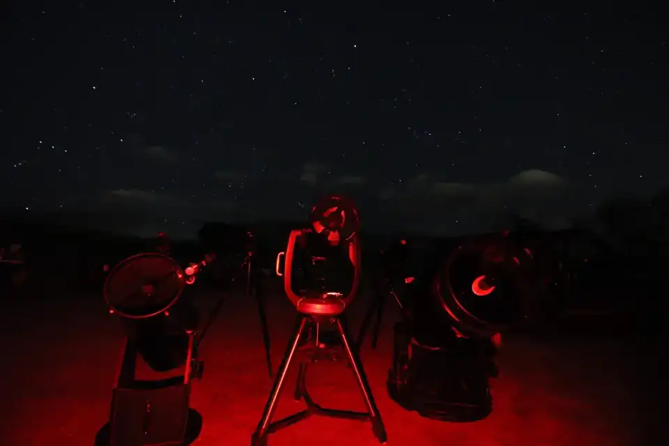 Several telescopes set up beneath the stars with red observing lights in an illustrative AstroTours.org field photograph.